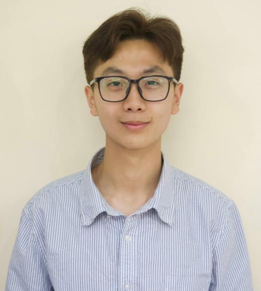 Young person wearing glasses, light blue button-up shirt, cream background